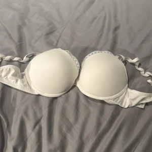 Vit bh från H&M - Säljer en vit bh från H&M med lätt vadderade kupor och spetsdetaljer upptill. Slät design som passar under toppar och klänningar. Perfekt för dig som vill ha en enkel och stilren bh.