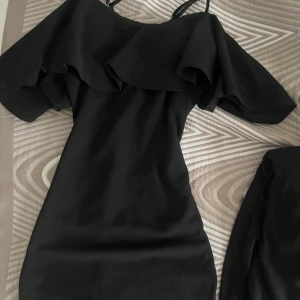 Svart offshoulder klänning med volang - Säljer en svart offshoulder klänning med bred volang upptill och smala axelband. Klänningen har en figurnära passform och är perfekt för dig som gillar stilrena plagg med en twist.