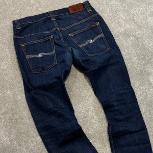 Nudie Jeans - Tjena! Säljer dessa schyssta mörkblå Nudie jeans! Jeansen är i fint skick, finns lagning i skrevet men de är gjort snyggt hos skräddare och syns inte utifrån (bild 5). Size 31/32, mått: 39cm midja, 100cm ytterbenslängd. Slimfit passform. Skriv vid funderingar!