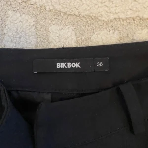 Svarta kostymbyxor från BikBok - Svarta kostymbyxor från BikBok med klassisk rak passform och diskret knäppning framtill. Perfekta för en stilren look och enkla att matcha med olika toppar.