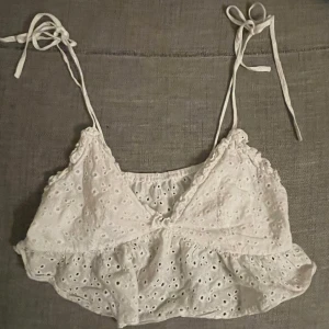 Vit broderad croppad linnetopp med volang - Söt vit croppad linnetopp med broderade hål och volangkant.