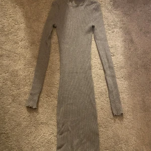 Grå ribbad långärmad klänning från FB Sister - Säljer en tight, grå ribbad långärmad klänning från FB Sister i storlek XXS. Klänningen har volangdetaljer vid hals och ärmslut samt en kroppsnära passform. Perfekt för dig som gillar en enkel men snygg stil.