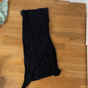 Svart långkjol från Amisu - Svart långkjol från Amisu i en mjuk och lätt polyester. Kjolen har omlott-design och en elegant slits framtill. Perfekt för dig som gillar en stilren och enkel look med en twist. Kan man också använda som klänning.