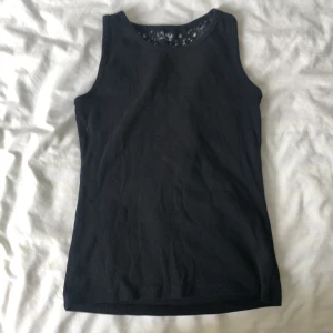 Svart linne - Svart ärmlös linnetopp från Next med rund halsringning. Baksidan har en snygg spetsdetalj upptill som ger toppen en extra touch. Perfekt att matcha med jeans eller kjol.