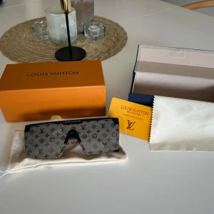 Svarta monogram-solglasögon från Louis Vuitton - Säljer ett par svarta solglasögon från Louis Vuitton med ikoniskt monogram-mönster över hela linsen. Modellen är oversized med rak, futuristisk form och diskret gulddetalj med logga upptill. Kommer med originalask, fodral och putsduk.