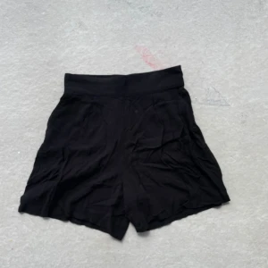 Svarta shorts med hög midja - Svarta shorts med hög midja och bred linning. De har en lös passform och är tillverkade i ett mjukt tyg som känns bekvämt mot huden. Perfekta för varma dagar och enkla att matcha med olika toppar.