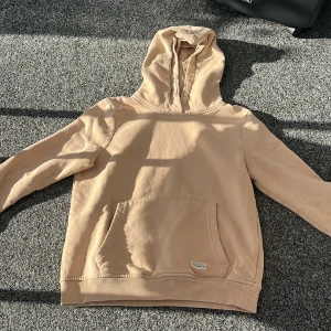 Beige hoodie från 157 välj pris - Säljer en beige hoodie från 157 med huva och magficka. Tröjan har ribbade muddar vid ärmslut och nederkant samt dragsko i huvan. Perfekt för en avslappnad och stilren look.