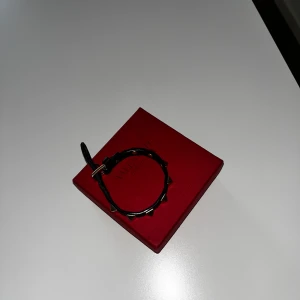 Svart armband med nitar från Valentino - Säljer ett svart armband från Valentino med guldiga nitar. Armbandet är gjort i skinn och har ett spänne för justering. Kommer med original ask och tygpåse. Perfekt accessoar för att lyfta din outfit. Tveka inte på att skicka o fråga
