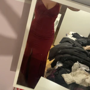 Röd balklänning med öppen rygg och slits - Säljer min gamla balklänning med smala axelband som korsas i ryggen. Klänningen har en tight passform, slits framtill och öppen rygg med snörning. Köpt från NK