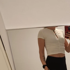 NY Vit croppad topp med rynk och nyckelhålsdetalj - Säljer en vit croppad topp med korta ärmar och snygg rynk framtill, aldrig använd. Toppen har en nyckelhålsöppning vid halsen och sitter tight. Perfekt till jeans eller kjol!