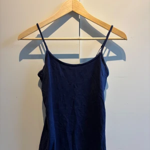 Mörkblå linnetopp med smala axelband - En enkel och stilren mörkblå linnetopp med smala axelband. Perfekt att matcha med jeans eller kjol för en avslappnad look. Tunt och mjukt material som känns skönt mot huden.