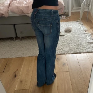 Blå bootcut jeans med låg midja - Säljer ett par klassiska blå bootcut jeans med låg midja och snygga detaljer vid fickorna. Jeansen har en lätt tvättad look och sitter tajt upptill men släpper ut vid benen. Perfekta för en avslappnad och trendig stil. Midjemått tvärs över är 38 cm och innerbenslängd 85. Skriv för fler frågor och bilder 💗
