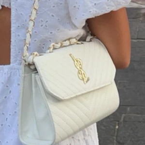 Vit axelväska från Yves Saint Laurent - Säljer en stilren vit axelväska från Yves Saint Laurent med guldfärgad logga framtill. Väskan har quiltad design och kedjerem med inslag av vitt material. Perfekt för att lyfta din outfit!