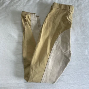 Beige ridbyxor från Pikeur - Snygga beige ridbyxor från Pikeur med helskodd design i äkta mocka i ljusare beige. Byxorna har dragkedja fram, bälteshällor och en liten ficka med dragkedja. Perfekta för ridning och har klassisk passform. I strl ungefär S-M