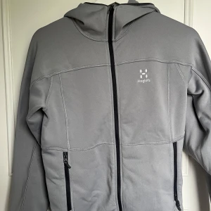 Grå hooded jacka från Haglöfs - Säljer en grå zip fleece med huva från Haglöfs. Jackan har hel dragkedja framtill och två fickor med dragkedja. Perfekt för lager-på-lager, använd ett fåtal gånger