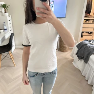 Vit t-shirt med svarta spetsdetaljer - Vit t-shirt med korta ärmar och svart spetskant vid ärmsluten. Super trendig och är fårn Zara. Storlek S. Använd en gång 