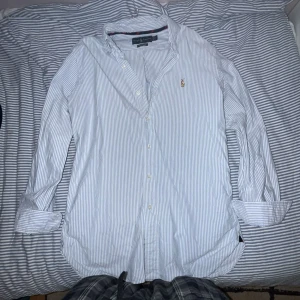 Blåvit randig skjorta från Ralph Lauren - Klassisk blåvit randig skjorta från Ralph Lauren med broderad logga på bröstet. Skjortan har lång ärm, knappar framtill och är i en klassisk passform. Perfekt för en stilren och tidlös look. 10/10 skick riktigt fet aldrig använt passar S-M
