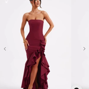 Bordeaux axelbandslös långklänning med volang - Säljer en elegant bordeaux axelbandslös långklänning från Babyboo. Klänningen har en tight passform, volangdetaljer längs slitsen framtill och en figurnära siluett. Perfekt för festliga tillfällen och bal.