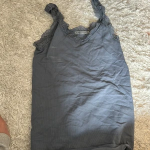 Grå linnetopp med spets från Soaked in Luxury - Säljer en grå linnetopp från Soaked in Luxury med fina spetsdetaljer längs axelbanden och urringningen. Perfekt att styla till jeans eller kjol för en enkel men snygg look.