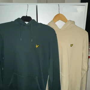 Beige hoodie från Lyle & Scott - Snygg beige hoodie från Lyle & Scott med klassisk gul logga på bröstet. Tröjan har huva med dragsko och en stor magficka framtill. Perfekt för en avslappnad stil.