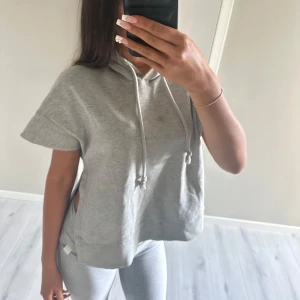 Grå kortärmad hoodie med slitsar - Säljer en ljusgrå hoodie med korta ärmar och huva med dragsko. Tröjan har slitsar i sidorna och är i mjukt sweatshirtmaterial. Pris kan diskuteras 