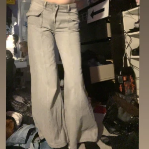 Ljusgråa vida jeansbyxor med små fickor  - Säljer ett par ljusgråa jeansbyxor med vida ben och små fickor framtill. Byxorna har hög midja och en klassisk jeanslook med en modern twist. Perfekta för dig som gillar en avslappnad och trendig stil.