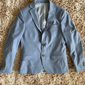 Ljusblå kostym från Dressmann - Säljer en ljusblå kostym från Dressmann i extra slim fit. Kavajen har två knappar framtill, klassiska slag och randigt innerfoder. Byxorna är raka och matchar kavajen perfekt. Perfekt för student eller sommarens fester.