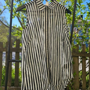 Svartvit randig ärmlös skjorta - Säljer en snygg ärmlös skjorta med svartvita ränder och klassisk krage. Skjortan har knappar hela vägen framtill och är tillverkad i ett lätt och luftigt material, perfekt för varma dagar.