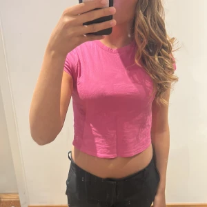 Rosa croppad t-shirt från Divided - Säljer en rosa croppad t-shirt från Divided H&M T-shirten har rund halsringning och korta ärmar. Perfekt för dig som gillar en enkel och stilren look med en poppig färg.