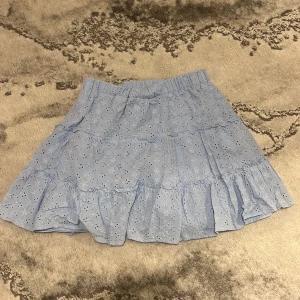 Ljusblå volangkjol från Sisters Point - Supersöt ljusblå kjol med broderade blommor och volanger från Sisters Point. Kjolen har resår i midjan och är perfekt för en somrig look. Den är kort och har ett romantiskt uttryck med sina fina detaljer.