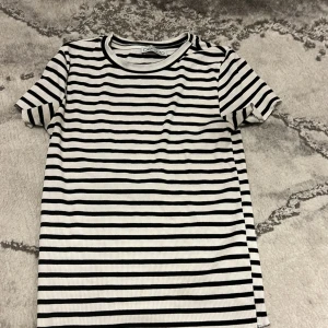 Randig t-shirt från DeFacto - Säljer en svartvit randig t-shirt från DeFacto. T-shirten har korta ärmar och är ribbad i materialet vilket ger en snygg struktur. Perfekt för en avslappnad och stilren look.