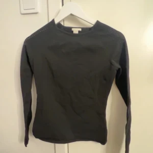 Svart långärmad tröja med detaljer vid axlarna - Säljer en svart långärmad tröja med små dekorativa hål längs axlarna. Tröjan har en tight passform och är enkel i designen, perfekt att matcha med olika outfits.