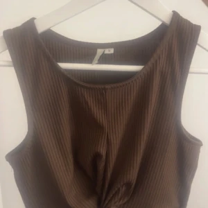 Brun ribbad linnetopp från NLY Trend - Säljer en brun ribbad linnetopp från NLY Trend. Toppen är ärmlös och har en twistad detalj framtill. Perfekt för att matcha med jeans eller kjol. Snygg och enkel design som passar till många tillfällen.