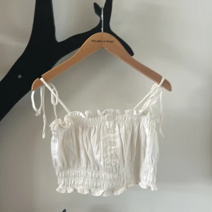 Vit croppad linnetopp från Designers Remix - Supersöt vit croppad linnetopp från Designers Remix med knytbara axelband, smockdetaljer och små knappar framtill. Toppen har volangkant upptill och nedtill för en extra touch. Perfekt för varma dagar! Endast använd 1 gång! Nypris 995kr på NK. Kom gärna med bud💞