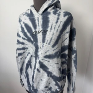 Grå och svart tie-dye hoodie  - Säljer en grå hoodie med svart tie-dye mönster från EVA. Tröjan har huva och en broderad logga framtill. Perfekt för en avslappnad stil och passar till det mesta. Storlek M och är i mycket bra skick😊