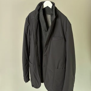 Svart kavaj från Z Zegna - Stilren svart kavaj från Z Zegna med klassisk krage och tre framfickor. Jackan har lång ärm och är tillverkad i polyesterblandning med en stickad insida som ger en modern look. Perfekt för dig som vill ha en dressad men avslappnad stil.