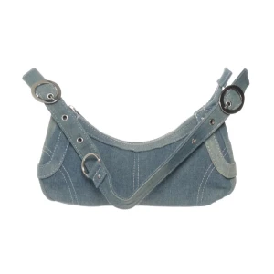 Blå axelväska i jeans - Säljer en blå axelväska i jeansmaterial med bred axelrem och stora silvriga ringdetaljer. Perfekt för dig som gillar denim och vill ha en unik accessoar till din outfit.