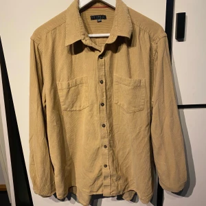 Beige manchester-skjorta från Critic - Säljer en beige långärmad skjorta i mjuk manchester från Critic. Skjortan har två bröstfickor och knäppning framtill. Perfekt för dig som gillar en avslappnad och klassisk stil.