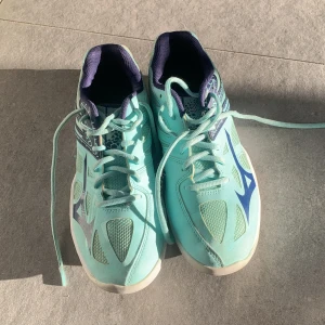 Mizuno inneskor - Säljer ett par turkosa sneakers från Mizuno med vita och mörkblå detaljer. Skorna har snörning och är tillverkade i syntetmaterial med meshpaneler för extra ventilation. Perfekta för träning eller vardag.