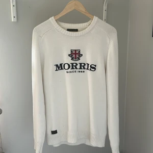 Vit stickad tröja från Morris - Vit stickad tröja från Morris med broderad logga och text på bröstet. Tröjan har rund halsringning och långa ärmar. Perfekt för en stilren och klassisk look.