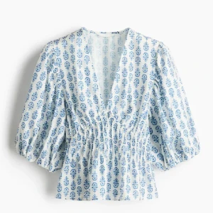 Vit och blå blus med mönster från H&M - Säljer en söt blus från H&M i vitt med blått blommigt mönster. Blusen har v-ringning, trekvartsärmar med resår och smockad midja som ger en fin passform. Perfekt för vår och sommar!