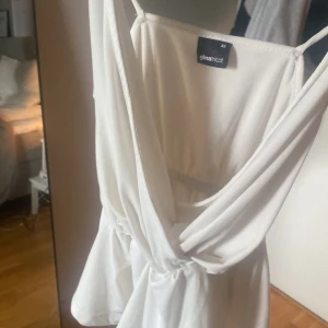 Vit topp från Gina Tricot - Säljer en söt vit omlottopp från Gina Tricot med smala axelband och volang nedtill. Toppen har en v-ringad omlottdesign och resår i midjan för en snygg passform. ❤️❤️