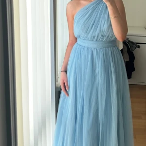 Ljusblå långklänning oneshoulder - Säljer en elegant ljusblå långklänning med oneshoulder-design och markerad midja. Klänningen har ett vackert fall och öppen rygg, perfekt för bal eller fest. 