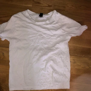Vit basic t-shirt - En enkel vit t-shirt med rund hals och korta ärmar. Modellen är rak och har en avslappnad passform. Perfekt att styla till jeans eller shorts för en clean look.