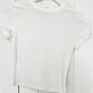 Vit croppad t-shirt - En enkel och stilren vit croppad t-shirt med rund halsringning och korta ärmar. Perfekt att matcha med jeans eller kjol för en clean look.