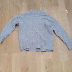 Grå stickad tröja från Lager 157, XS - Mysig grå stickad tröja från 157 i storlek XS. Tröjan har en rak passform, ribbad halsringning och långa ärmar. Perfekt för lager-på-lager och enkel att matcha med jeans eller kjol. Stilren och enkel design som funkar till allt.