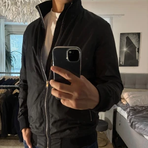 Svart bomberjacka Selected Homme M - Svart bomberjacka från Selected Homme i storlek M. Jackan har dragkedja framtill, ribbade muddar och krage samt fickor med dragkedja. Tillverkad av återvunna fibrer och har en clean, stilren look som passar perfekt till jeans och sneakers.