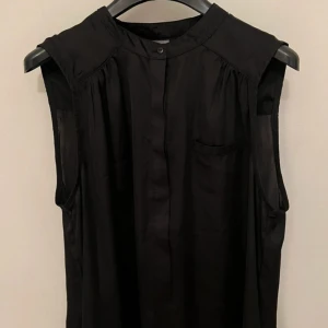 Svart ärmlös klänning Gina Tricot - Svart, ärmlös klänning från Gina Tricot i lätt och flowigt polyestertyg. Enkel design med dold knappslå framtill, liten bröstficka och rundad hals. Använd men i mycket bra skick. 