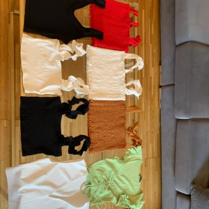 Färgglada croppade toppar & omlottopp - Säljer flera croppade toppar i svart, vitt, rött och brunt med breda axelband och smockdetaljer, samt en ljusgrön omlottopp med knyt och volangdetaljer. Perfekta för sommaren och att mixa olika stilar. Alla toppar är ärmlösa utom den gröna som har kort ärm. Xs/S, helt nya, 55 kr för en, 300 för alla