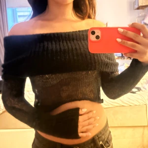 Svart offshoulder stickad croppad tröja - Säljer en svart stickad tröja med offshoulder-modell och croppad passform. Tröjan har långa ärmar och bred ribbad kant upptill. Den är tunnstickad och lite transparent, perfekt för en trendig look. 